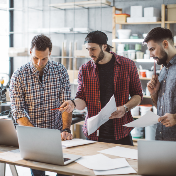 three men over a drafting table and laptop